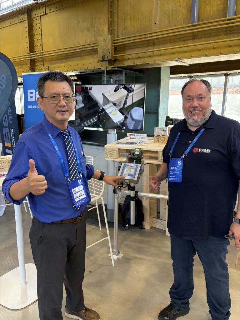 Two men giving thumbs up next to industrial printing equipment.