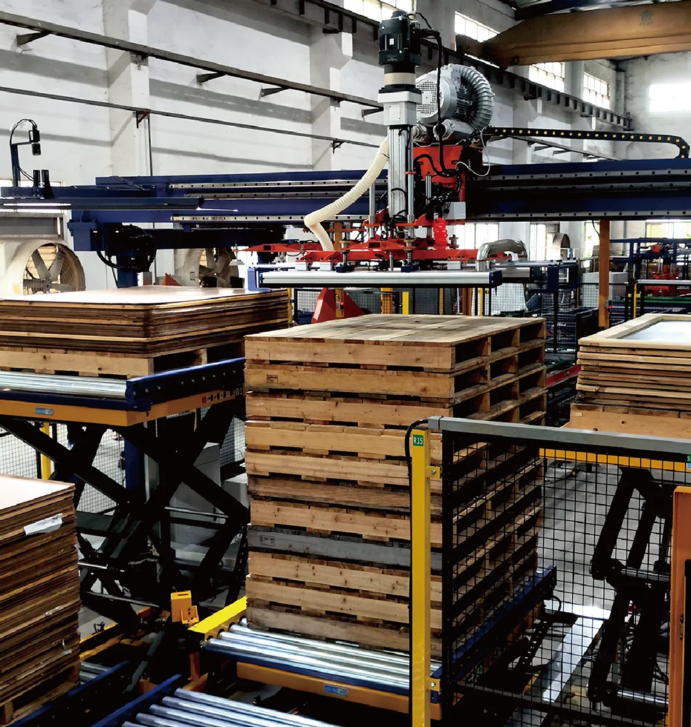 Industrial gantry robot stacking wooden pallets in a factory.