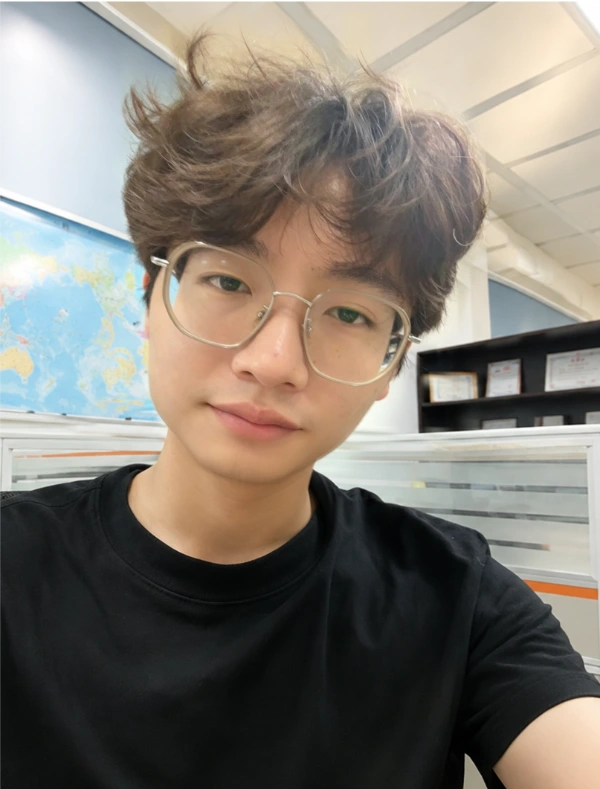 Young man with wavy brown hair and glasses in office.